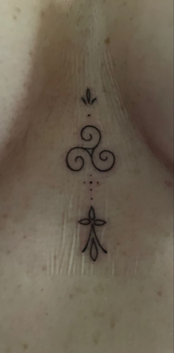 the back of a woman's neck with an ornamental tattoo design on her left side