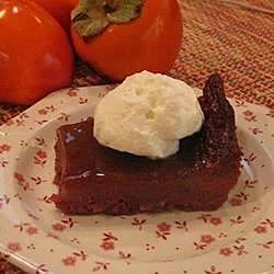 a piece of chocolate cake on a plate with whipped cream and tomatoes in the background