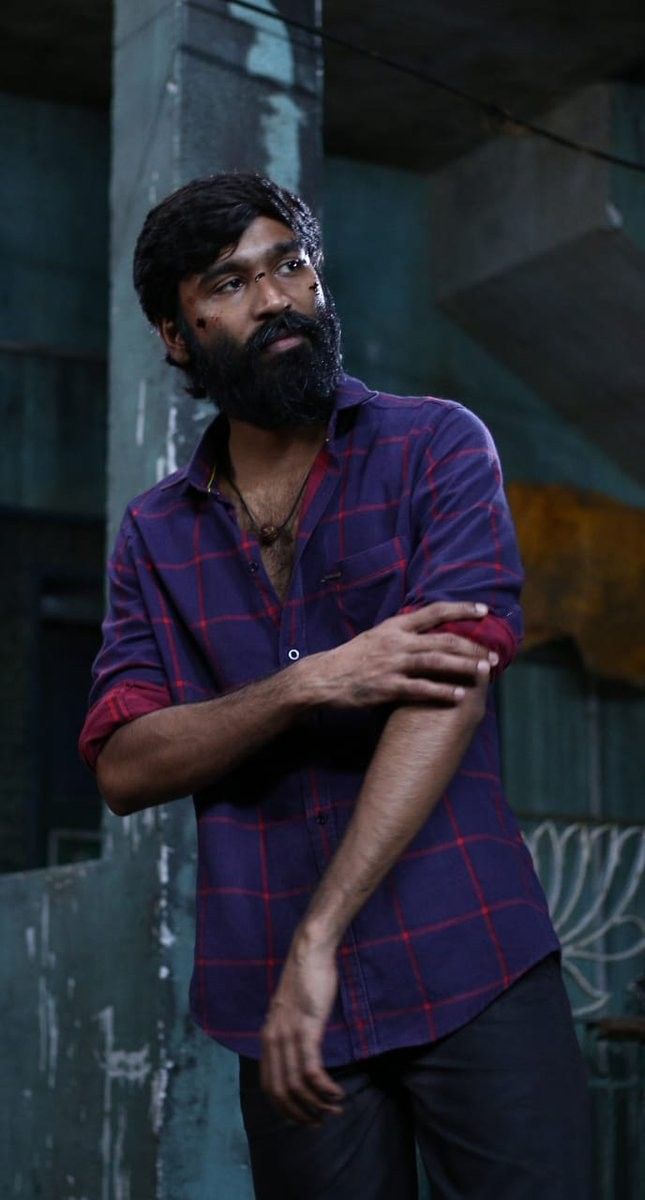 a man with a long beard standing in front of a wall and holding his arms crossed