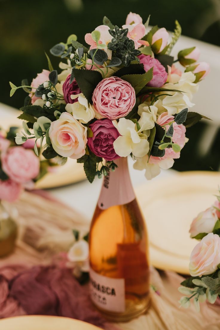 a vase filled with pink and white flowers on top of a table next to plates