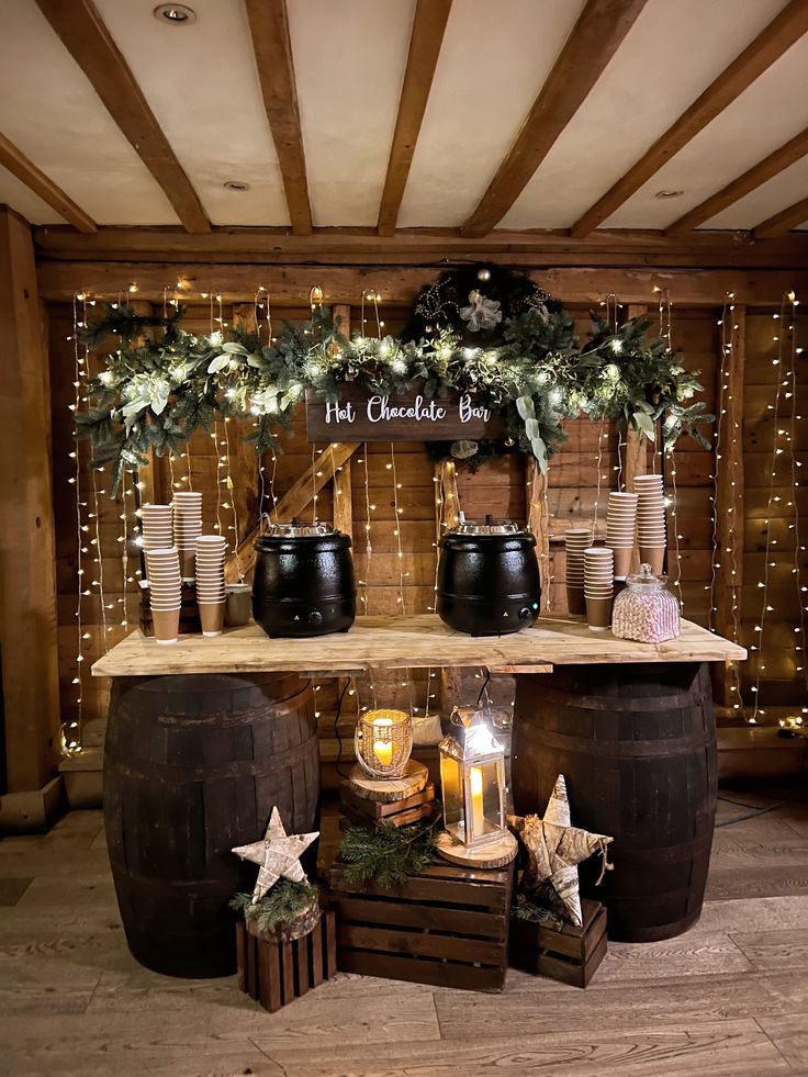 a wooden table topped with barrels filled with candles and greenery next to potted plants