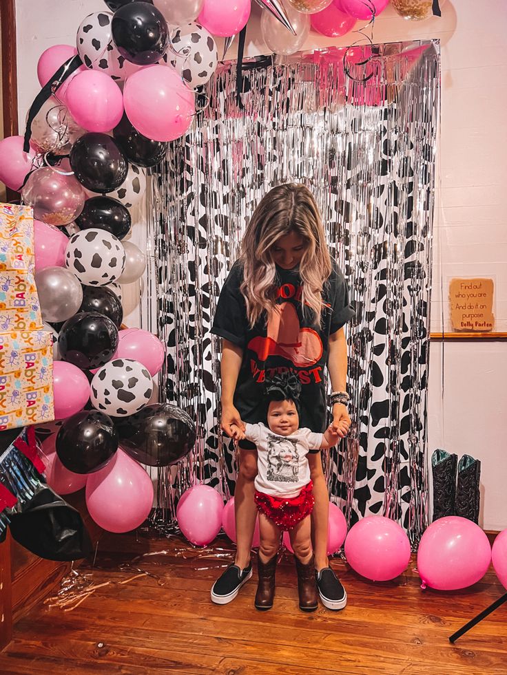 a woman holding a child in front of a balloon wall with pink and black balloons