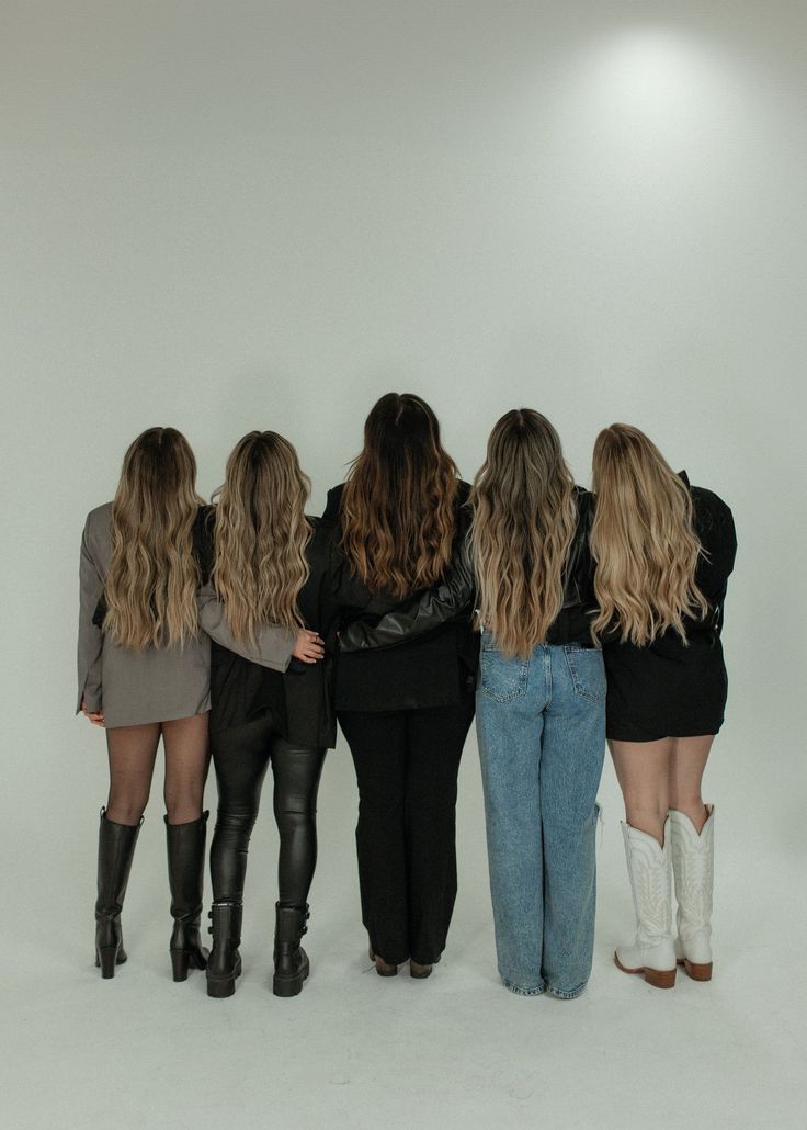 four women are standing in front of a white wall with their backs to the camera