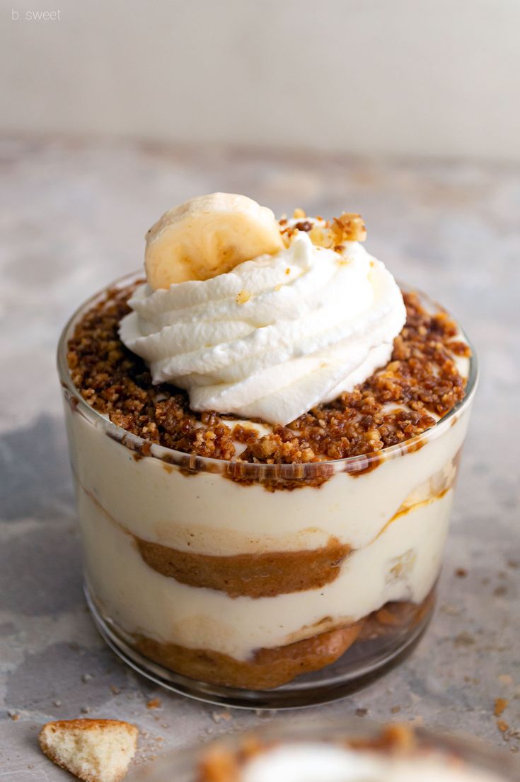 a dessert in a glass dish topped with whipped cream, banana and walnut crumbs