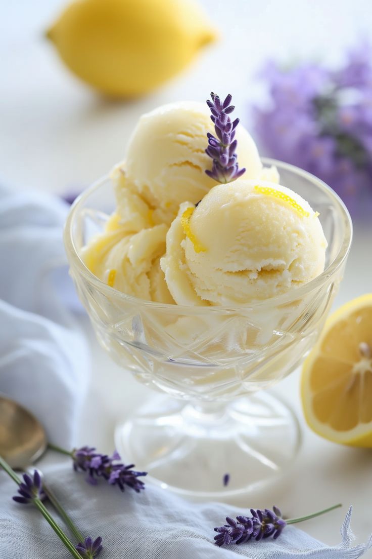 two scoops of ice cream in a glass bowl with lavender sprigs next to it