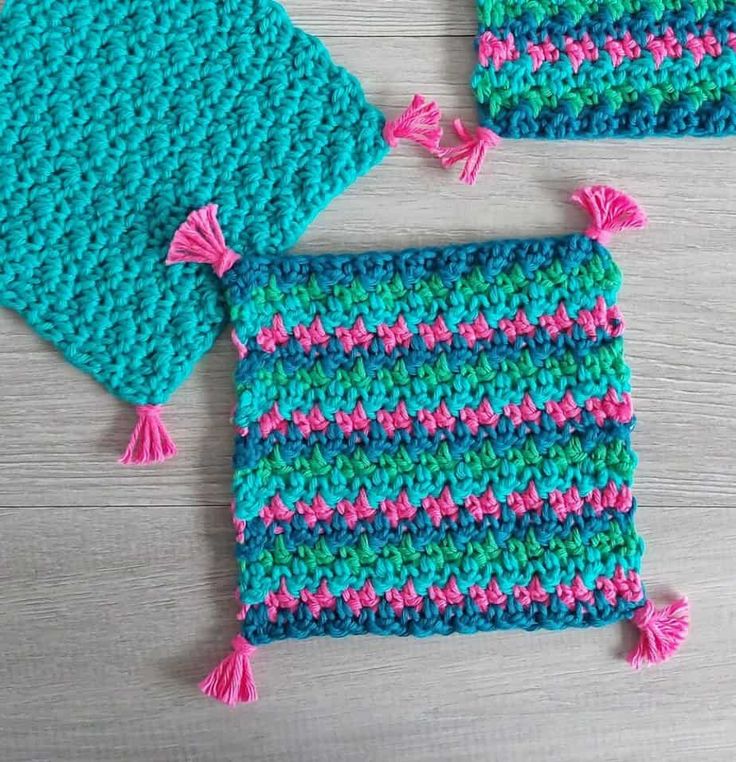 two crocheted potholders with tassels on the sides and one in blue, pink and green