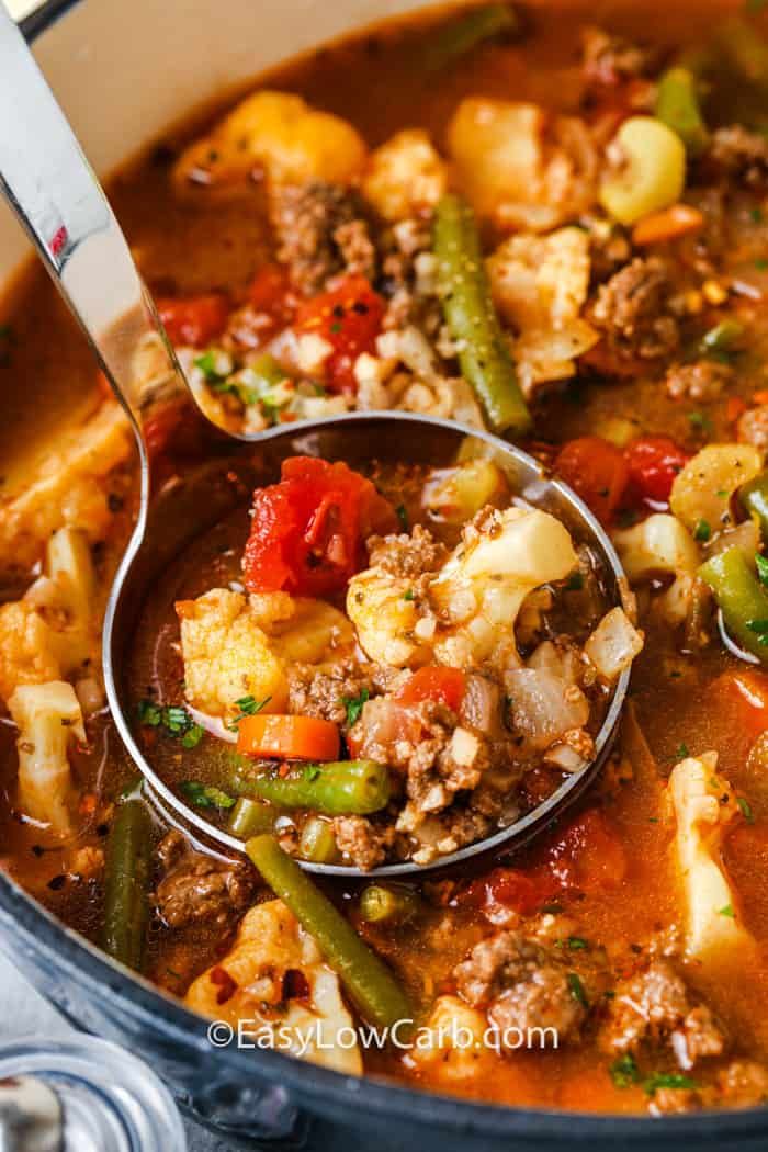 a ladle full of soup with vegetables and meat