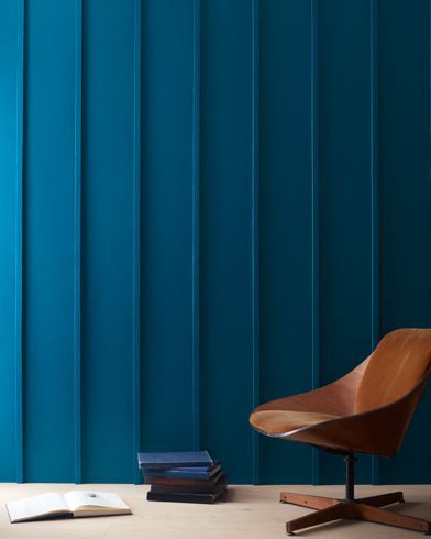 a chair and some books on a table in front of a blue wall with vertical stripes