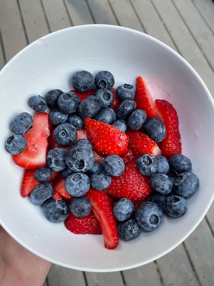 a white bowl filled with blueberries and strawberries on top of a wooden table