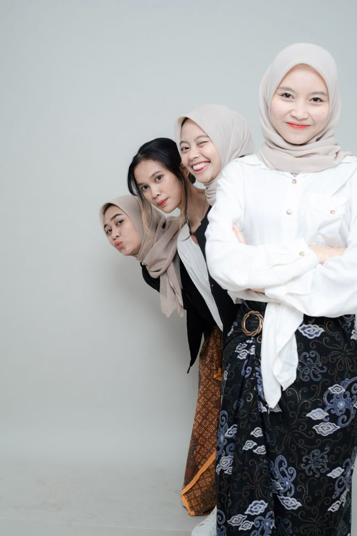 three women standing next to each other in front of a white wall with their arms crossed