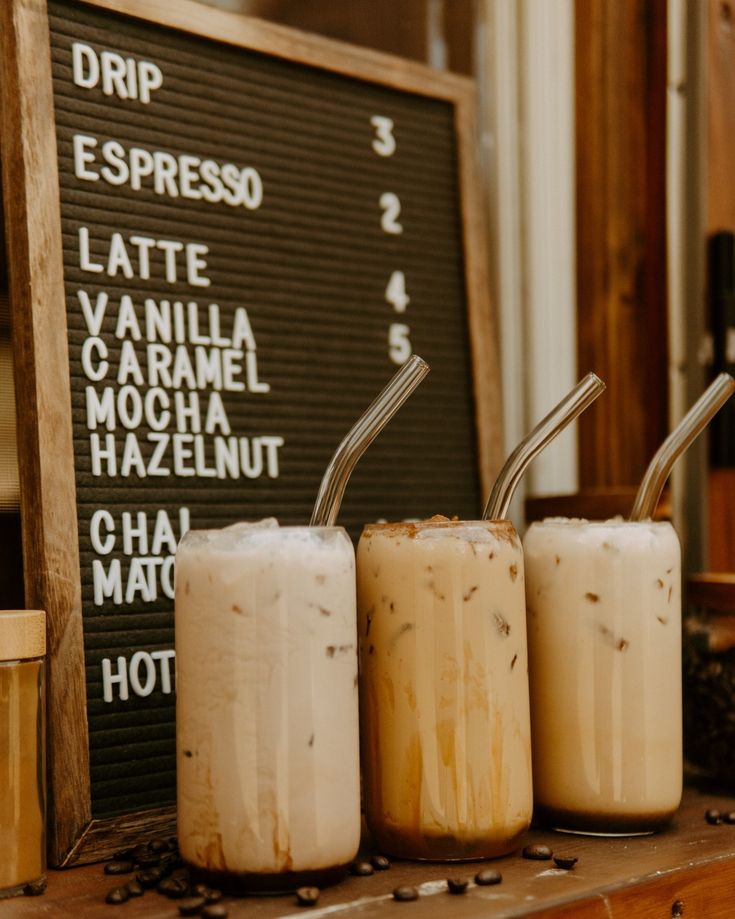 three drinks sitting on top of a counter next to a chalk board with writing on it