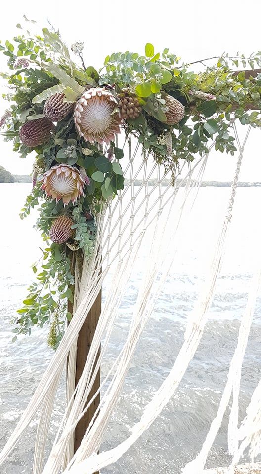 an arrangement of flowers and greenery is tied to a wooden pole on the beach