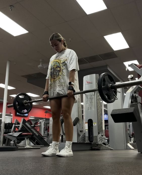 a woman standing in the middle of a gym holding a barbell