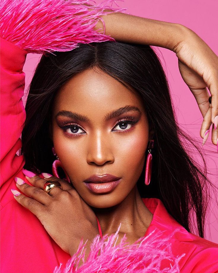 a woman with pink feathers on her head and hands behind her head, posing for the camera