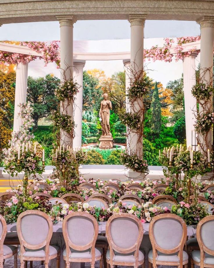 an outdoor wedding setup with chairs and flowers on the table in front of a statue