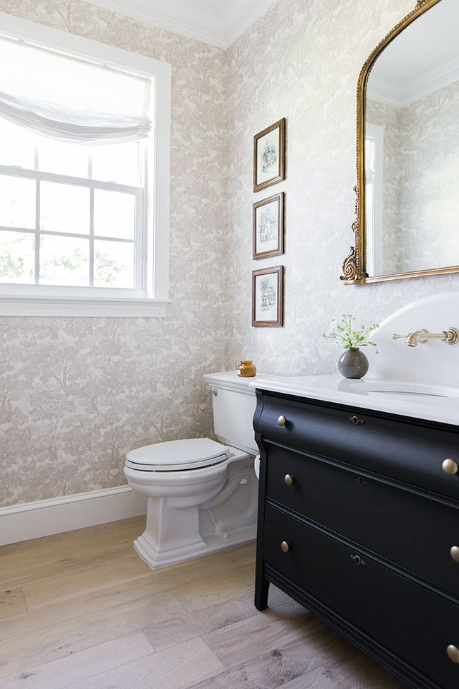 a white toilet sitting next to a black dresser in a bathroom on top of a hard wood floor