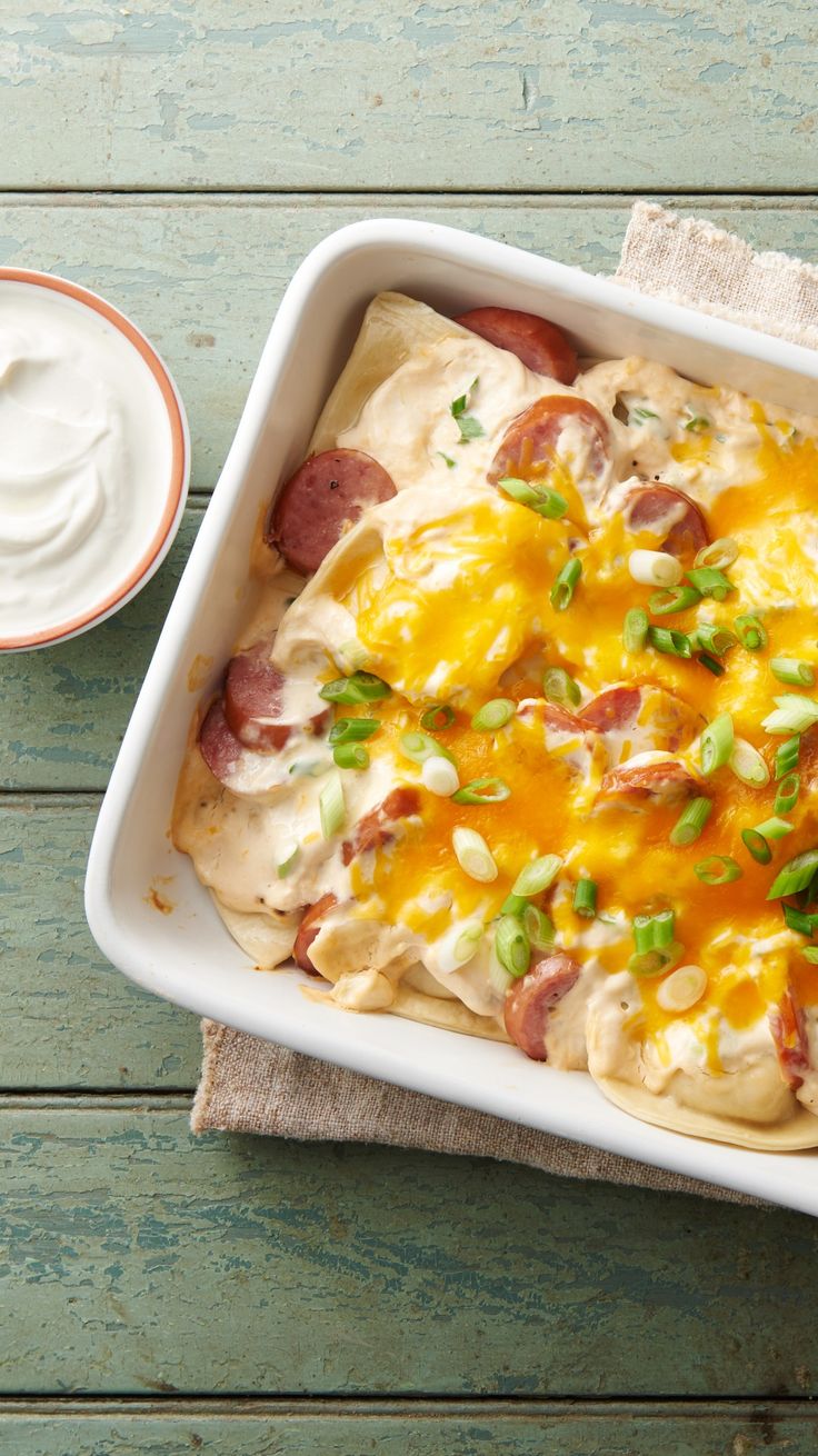 a square casserole dish with cheese, bacon and green onions on it next to a cup of sour cream