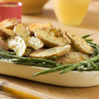 green beans and potatoes in a dish on a wooden table next to a glass of orange juice