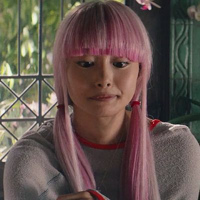 a woman with pink hair and bangs sitting in front of a window looking at the camera