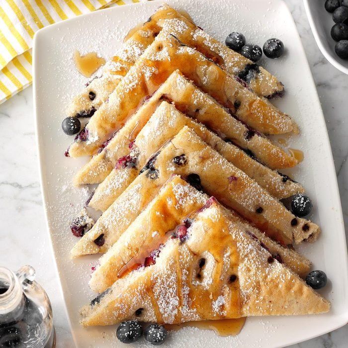 blueberry crepes with powdered sugar and syrup on a white platter