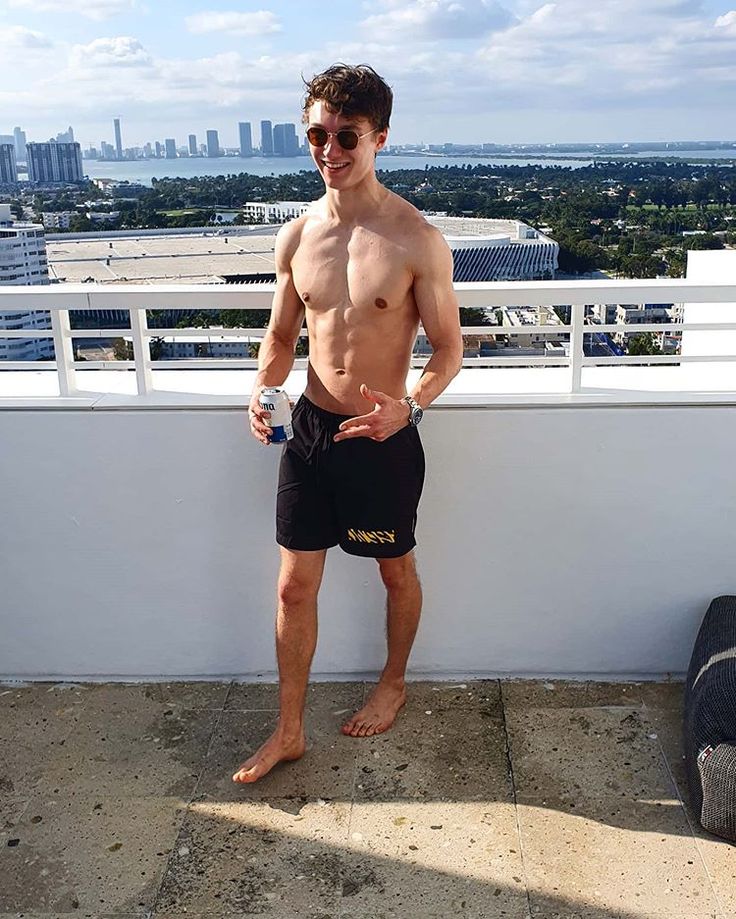 a shirtless man standing on top of a roof next to a water bottle and sunglasses