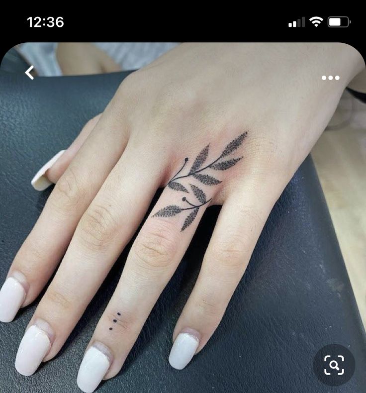 a woman's hand with a small leaf tattoo on her left ring finger,