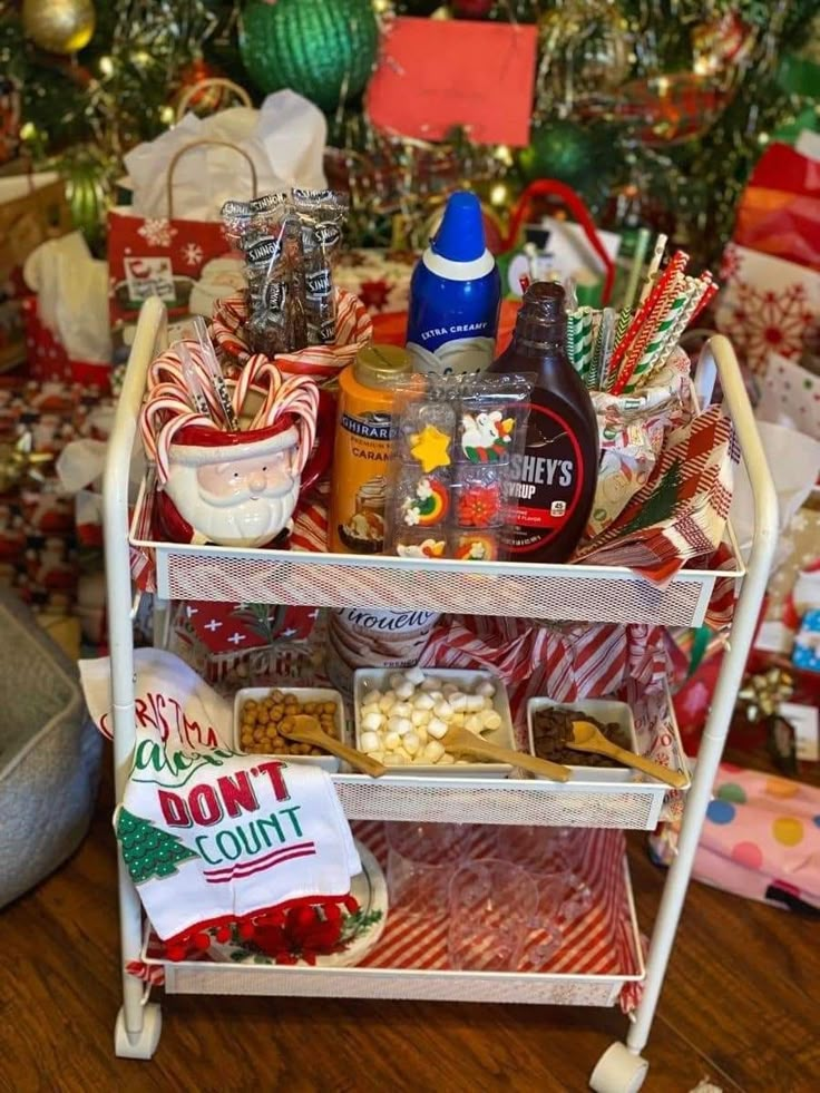 a white cart filled with lots of holiday food and condiments next to a christmas tree