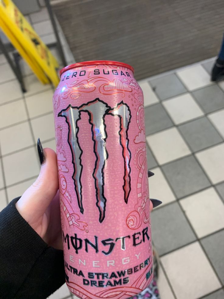 a person holding up a pink monster energy drink in front of a checkered floor