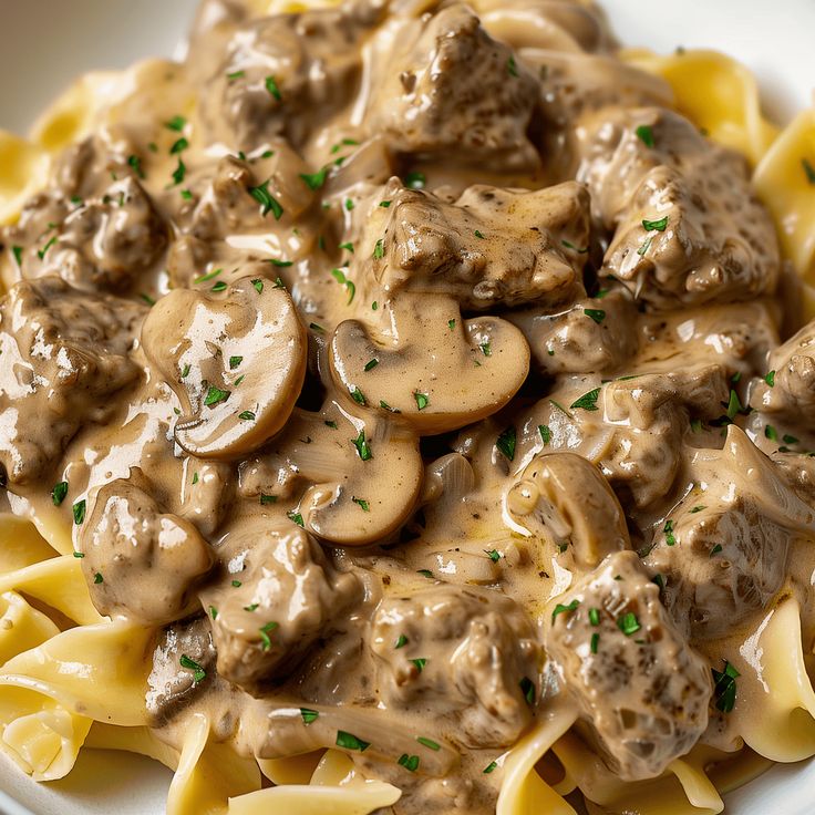 a white plate topped with pasta covered in meat and mushroom stroganone sauce