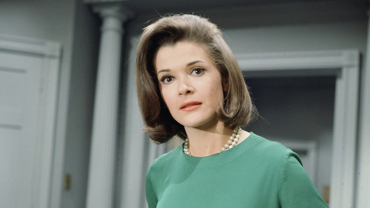 a woman in a green dress and pearls on her neck is looking off to the side