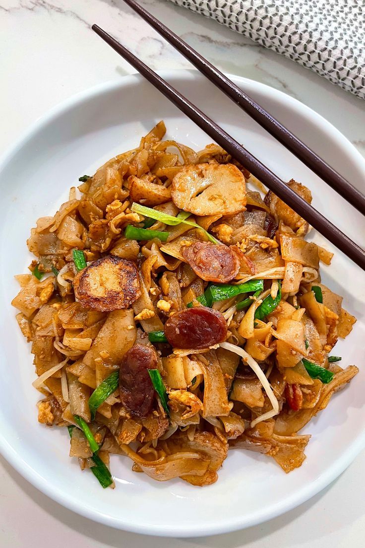 a white plate topped with stir fry and chopsticks