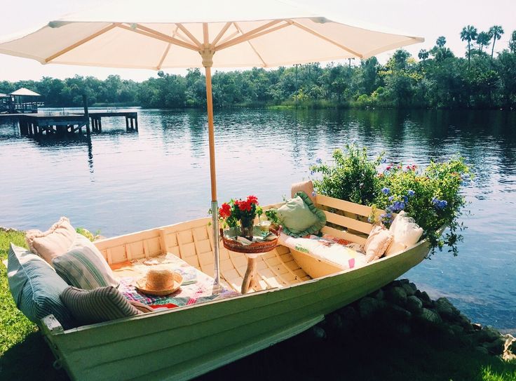 a wooden boat with an umbrella on the grass next to some flowers and plants in it