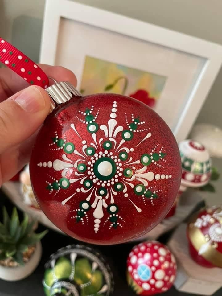 a hand holding a red ornament with green and white designs on it next to other ornaments