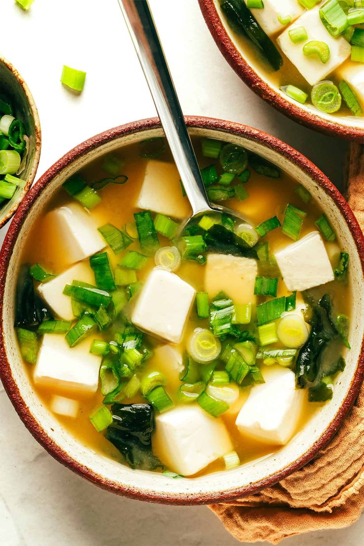 two bowls of soup with tofu, green onions and celery on the side