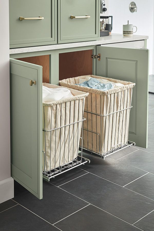 two baskets in the middle of a kitchen with green cupboards and tile flooring