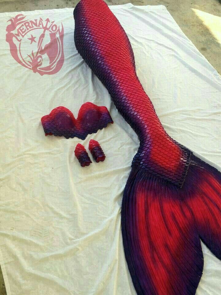 a purple and red mermaid tail laying on top of a white sheet next to pieces of plastic