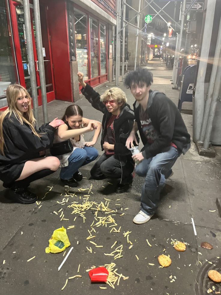 four young people sitting on the ground in front of a building with food all over it