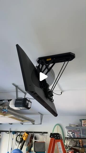 an overhead television mounted to the ceiling in a garage with tools hanging from it's sides