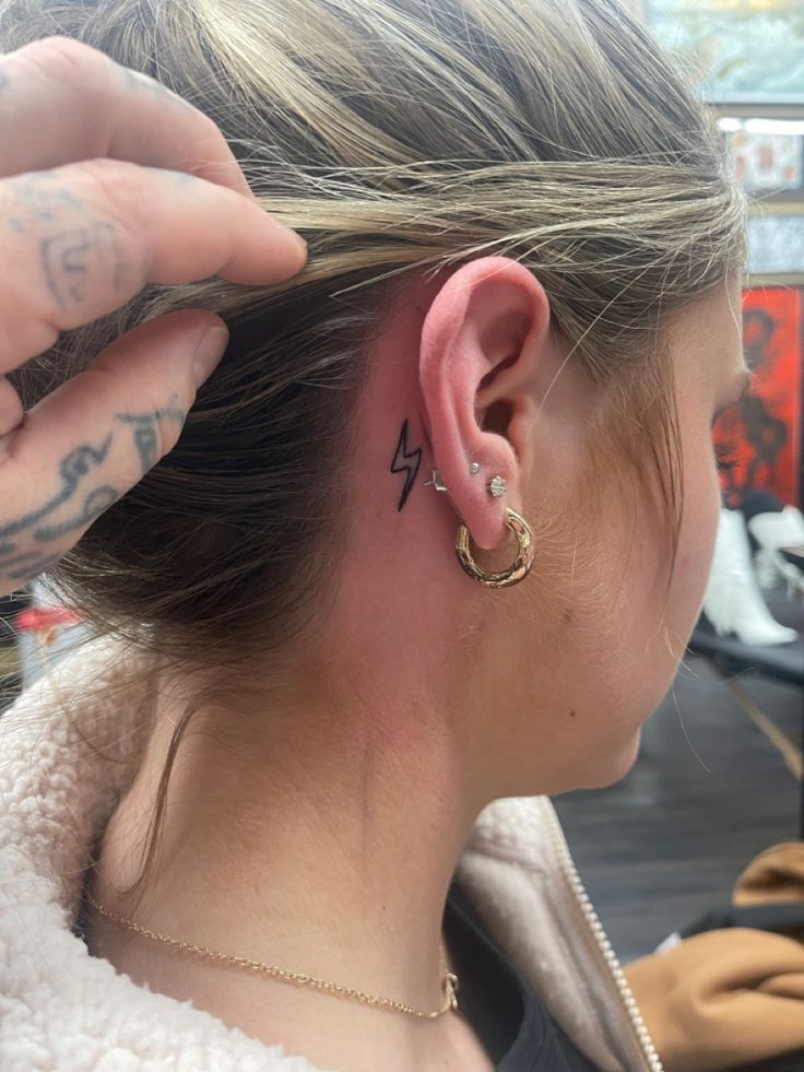 a woman with tattoos on her left ear and behind her ear is a small gold hoop