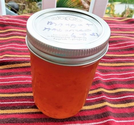 a jar of jam sitting on top of a red and yellow table cloth next to a white chair