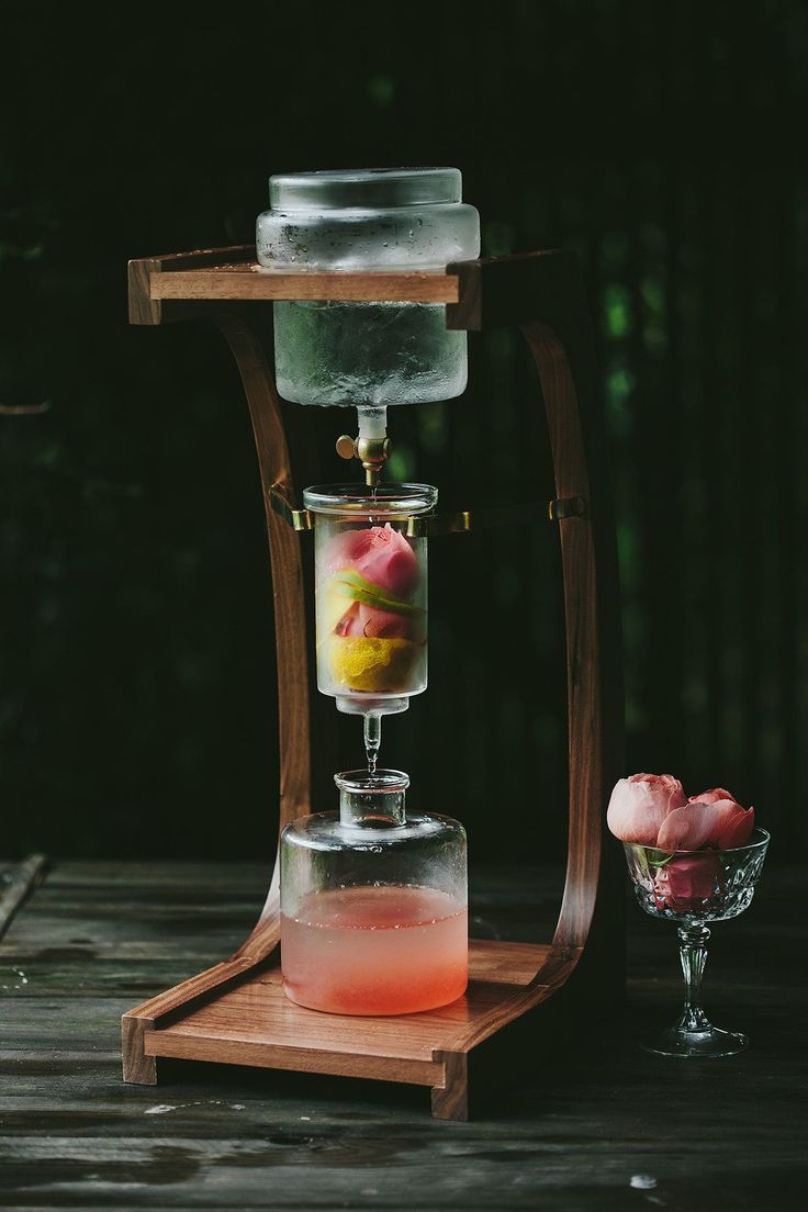 a drink dispenser filled with liquid on top of a wooden table next to a glass vase