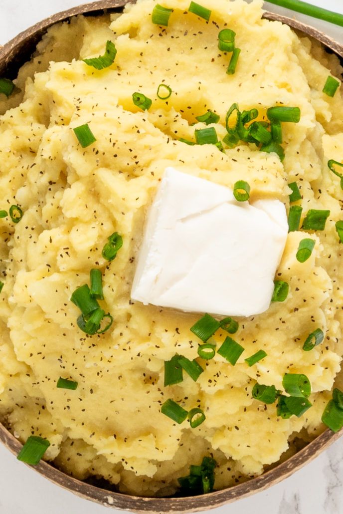 mashed potatoes with green onions and parmesan cheese in a bowl on a marble surface