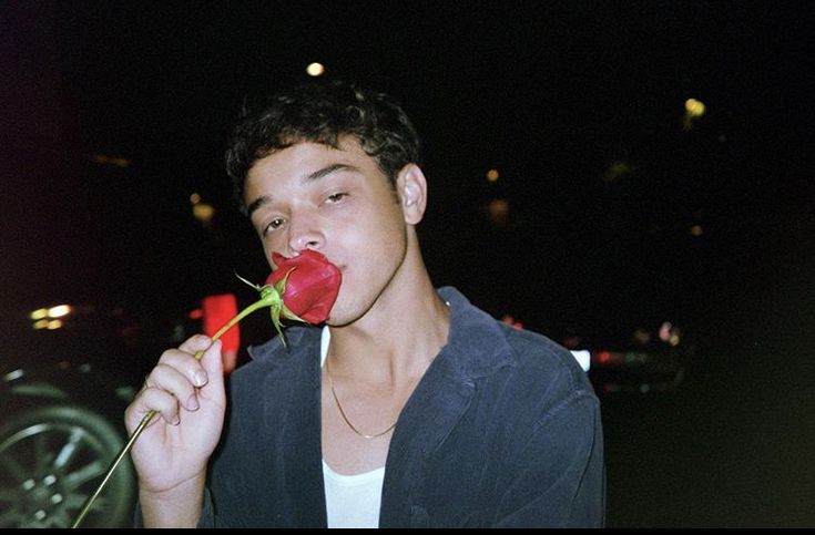 a young man holding a red rose in his mouth