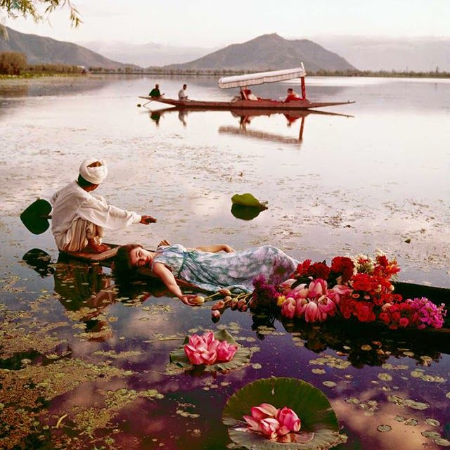 two people floating on top of a body of water next to flowers and canoes