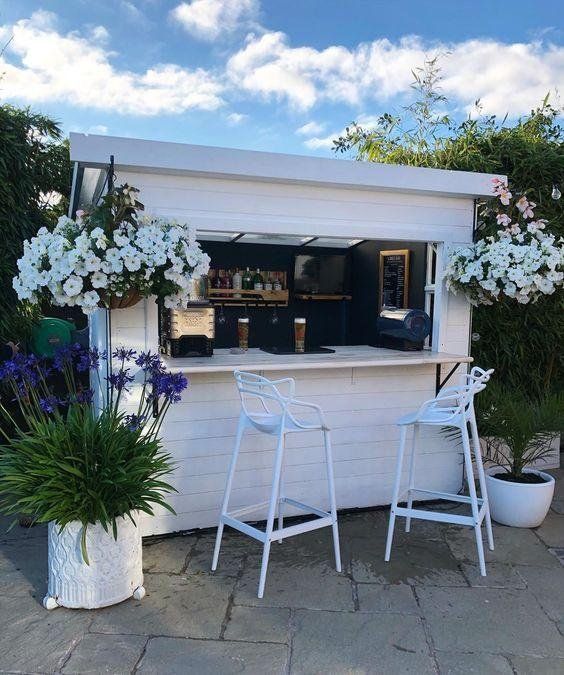 an outdoor bar with white chairs and flowers on the outside, next to potted plants