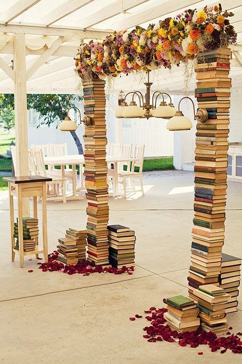 a bunch of books stacked on top of each other under a white tent covered in flowers