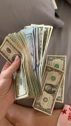 a person holding money in their hand on top of a couch next to a pile of cash