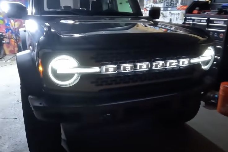 the front end of a black truck with its lights turned on in a garage area