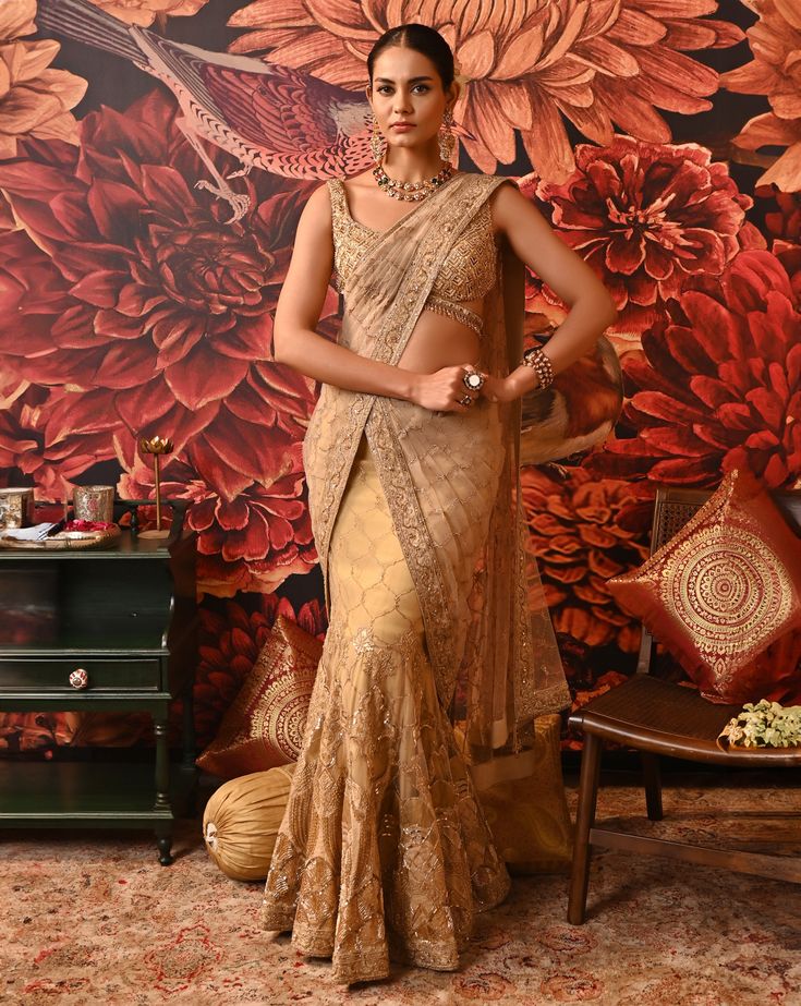 This authentic Layla saree is a one-of-a-kind attire that exudes glamour and modernity. The fishtail drape on the skirt adds a contemporary twist to your classic saree. The vivid embroidery details highlighted with beads are fascinating along with the attached sheer pallu. The sleeveless blouse is heavily accentuated with beads and sequins. A great show-stealer with a style so surreal. Heavily embellished cross-band sleeveless gold-foil printed blouse with centre back hook opening Fish-cut Saree with embroidered applique work with dabka and nakshi at the border of the pallu Side zip closure in the saree. From Moledro’s Riwayat collection. DELIVERY TIMEPlease allow 8-12 weeks for your outfit to arrive. FABRIC DETAILSSaree - Butterfly Net, Zari BrocadePallu - Butterfly NetBlouse - Cotton Sil Transitional Tissue Silk Sharara For Reception, Gold Floor-length Pre-draped Saree With Cutdana, Resham Embroidery Saree With Side Open, Transitional Season Raw Silk Pre-draped Saree, Transitional Season Pre-draped Raw Silk Saree, Bollywood Style Art Silk Pre-draped Saree With Sheer Dupatta, Festive Pre-draped Saree With Sheer Dupatta In Tissue Silk, Bollywood Style Pre-draped Tissue Silk Saree For Reception, Gold Pre-draped Saree For Reception