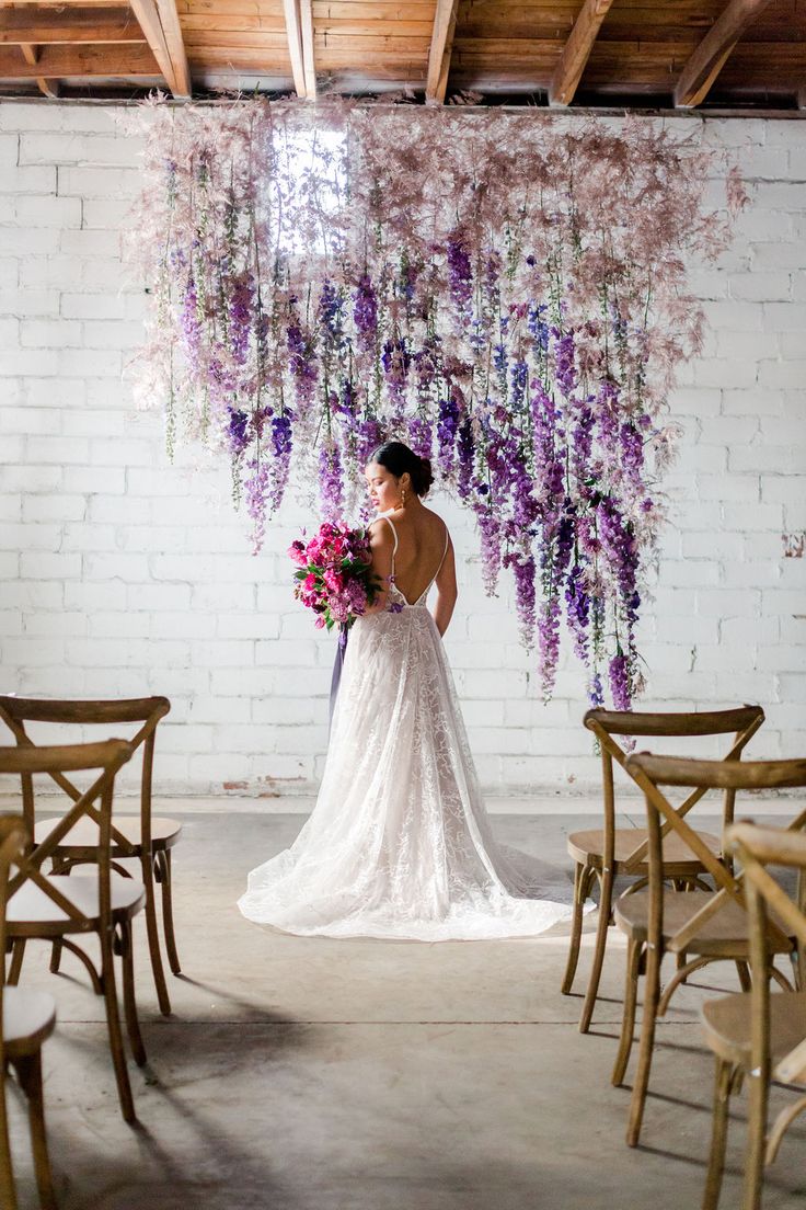 a woman in a wedding dress standing next to chairs with flowers hanging from the ceiling